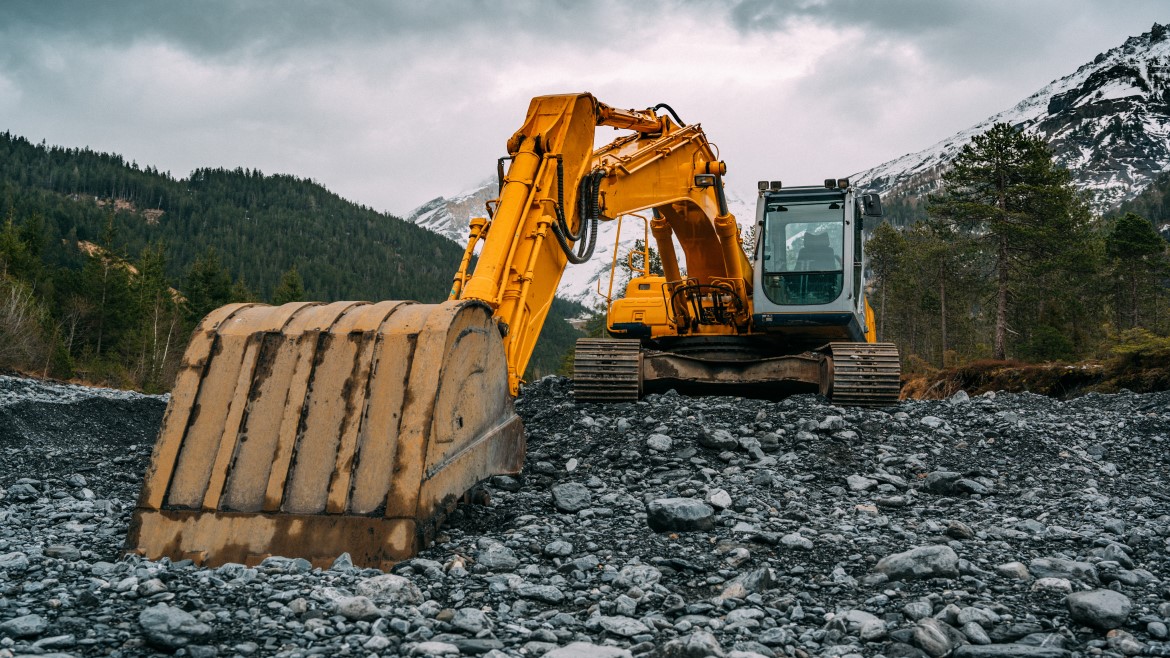 Why Hydrolytic Stability Matters in Hydraulic Fluid Formulations Excavator vehicle digging into rocky material in an area surrounded by mountains and trees