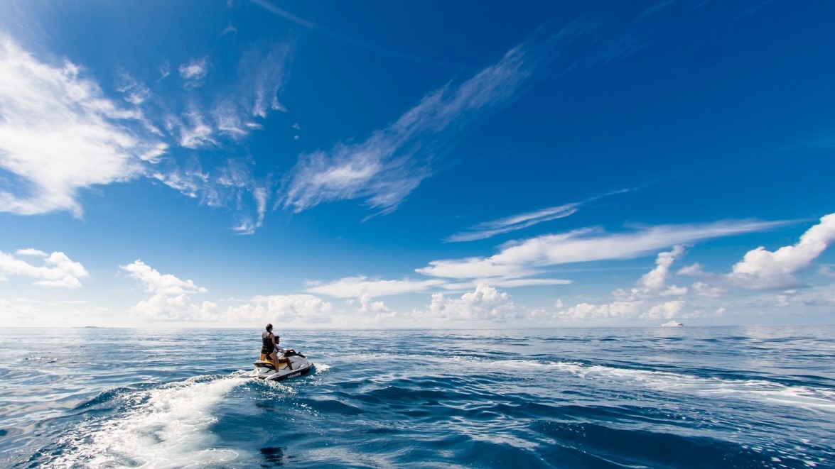 Ocean scene with jet ski rider headed toward horizon with blue sky above