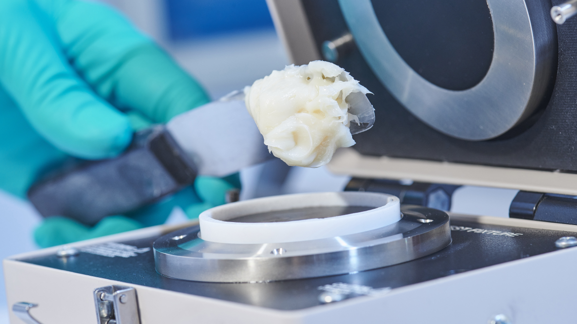 Close view of a gloved hand near lab equipment holding a tool with a sample of industrial grease 