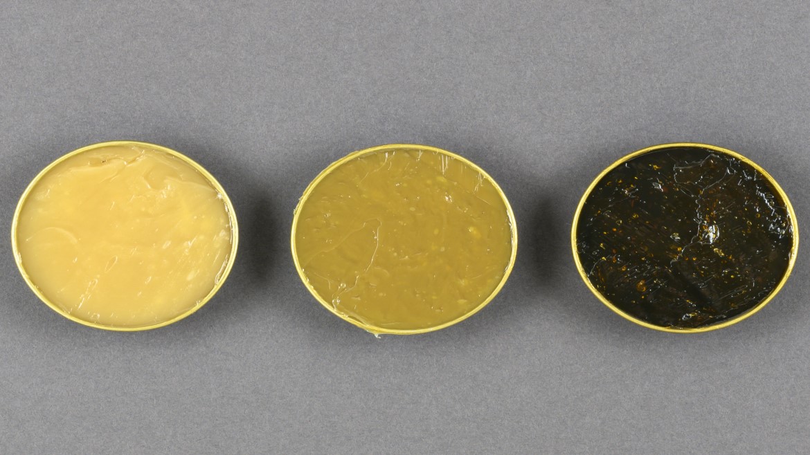 three circular containers in a row filled with industrial greases in bright yellow on the left, dark yellow in the center and black on the right