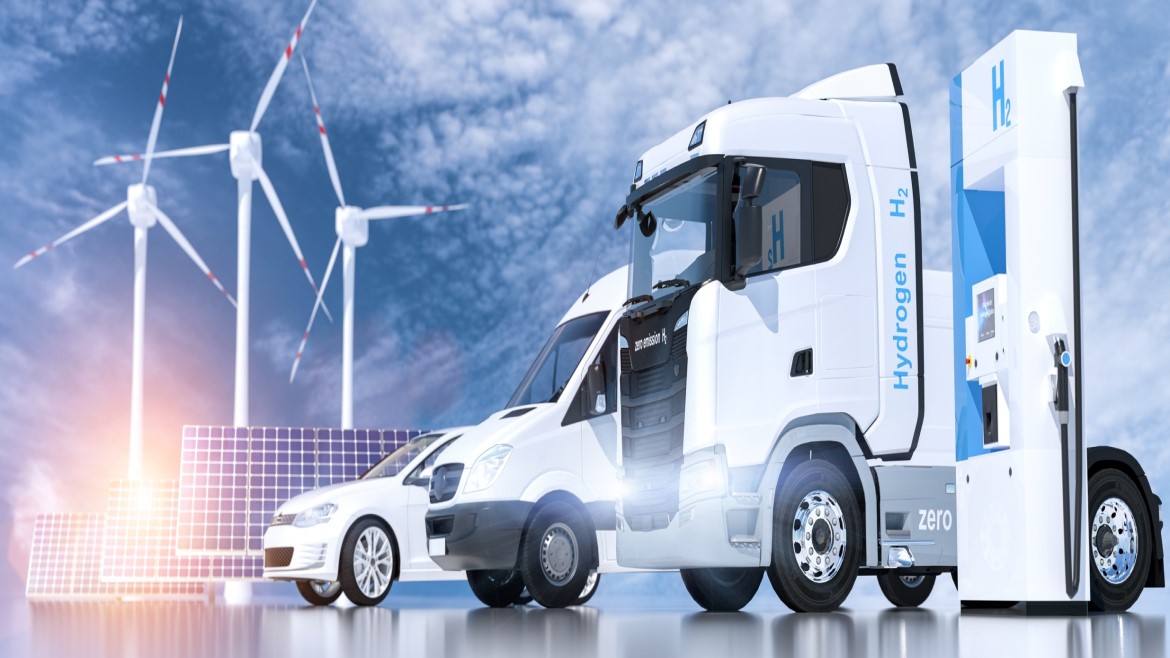 Wind turbine, solar panels, a car, van and heavy-duty truck lined up with clouds in the background