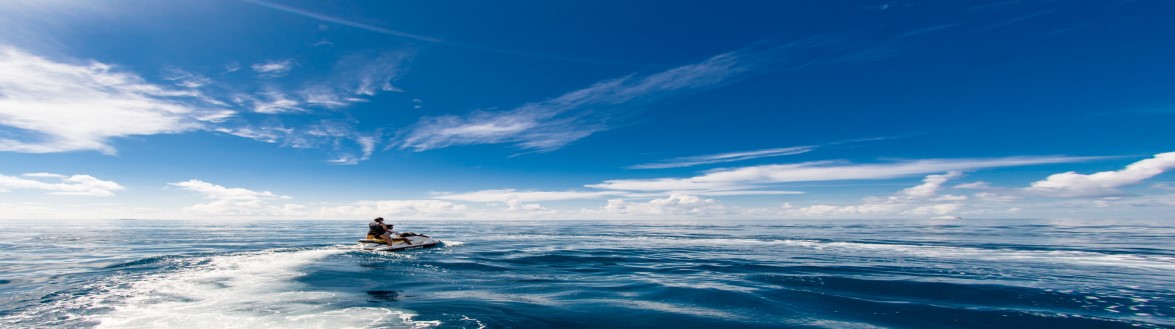 Ocean scene with jet ski rider headed toward horizon with blue sky above