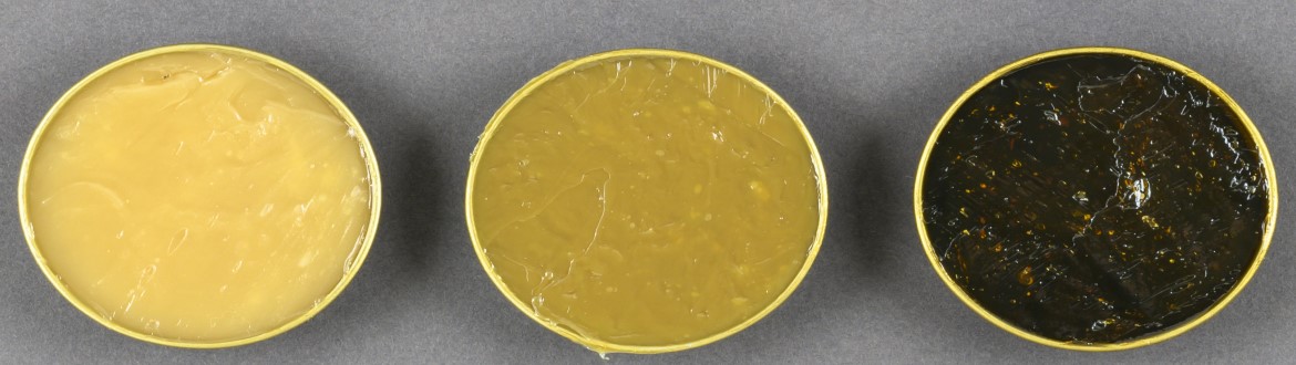 three round containers of grease of various colors lined up in a row with bright yellow on the left, dark yellow in the center and black on the right