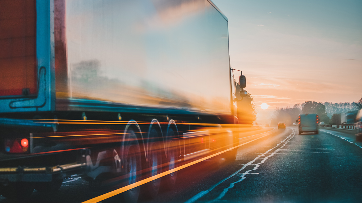 Heavy duty truck traveling on a highway away from the camera and toward a setting sun